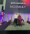 To personer står på en scene foran en stor skjerm med teksten Ignite expands to Norway.