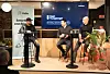 Tre personer sitter på høye stoler på en scene og deltar i en paneldebatt foran publikum.