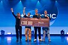 Gruppe på scene holder en stor sjekk på 300 000 euro foran blå bakgrunn.
