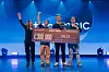 Gruppe på scene holder en stor sjekk på 300 000 euro foran blå bakgrunn.